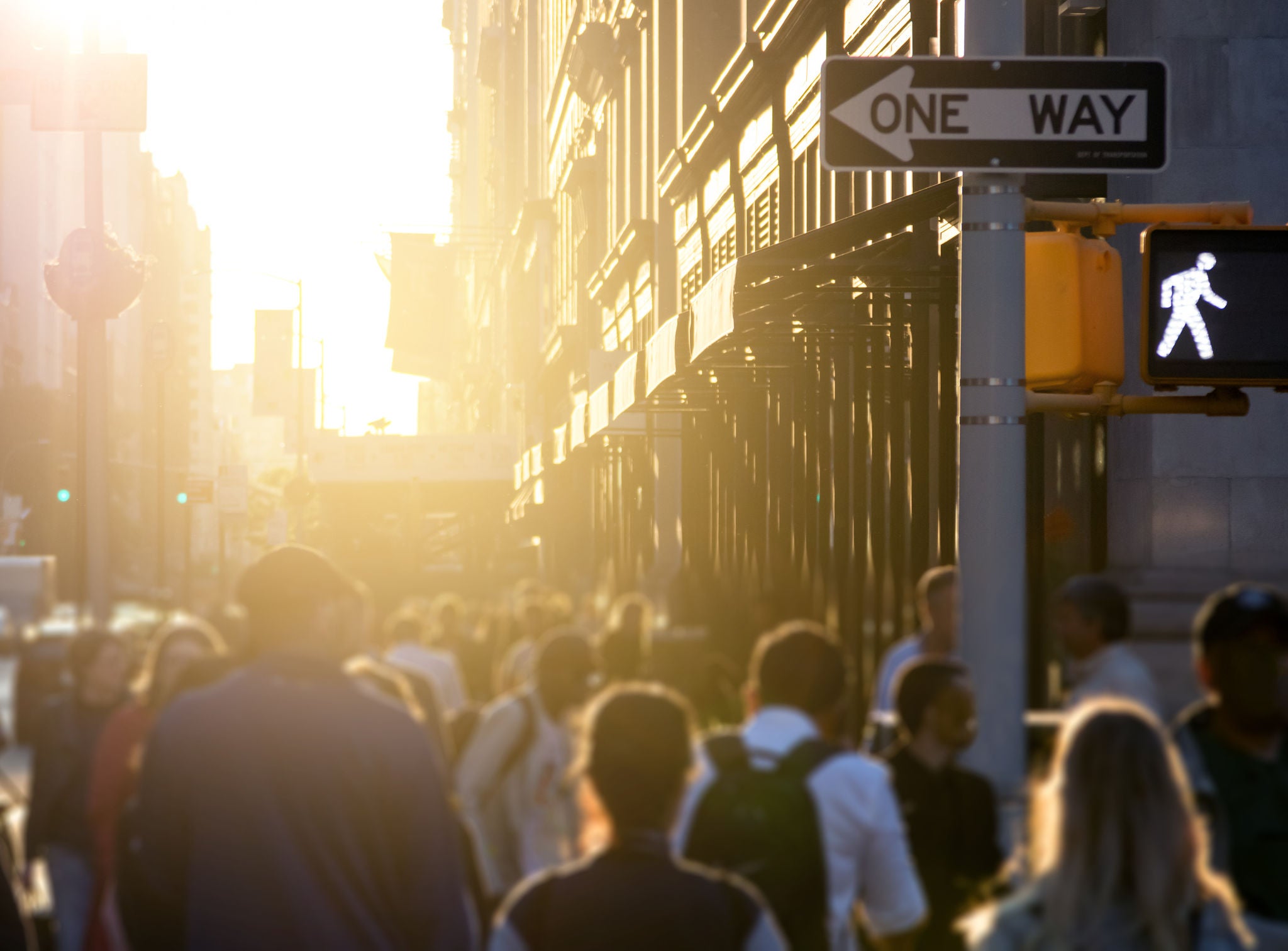 Crowd of anonymous people walking down the sidewalk with bright sunlight in the background on a busy street in Midtown Manhattan, New York City NYC