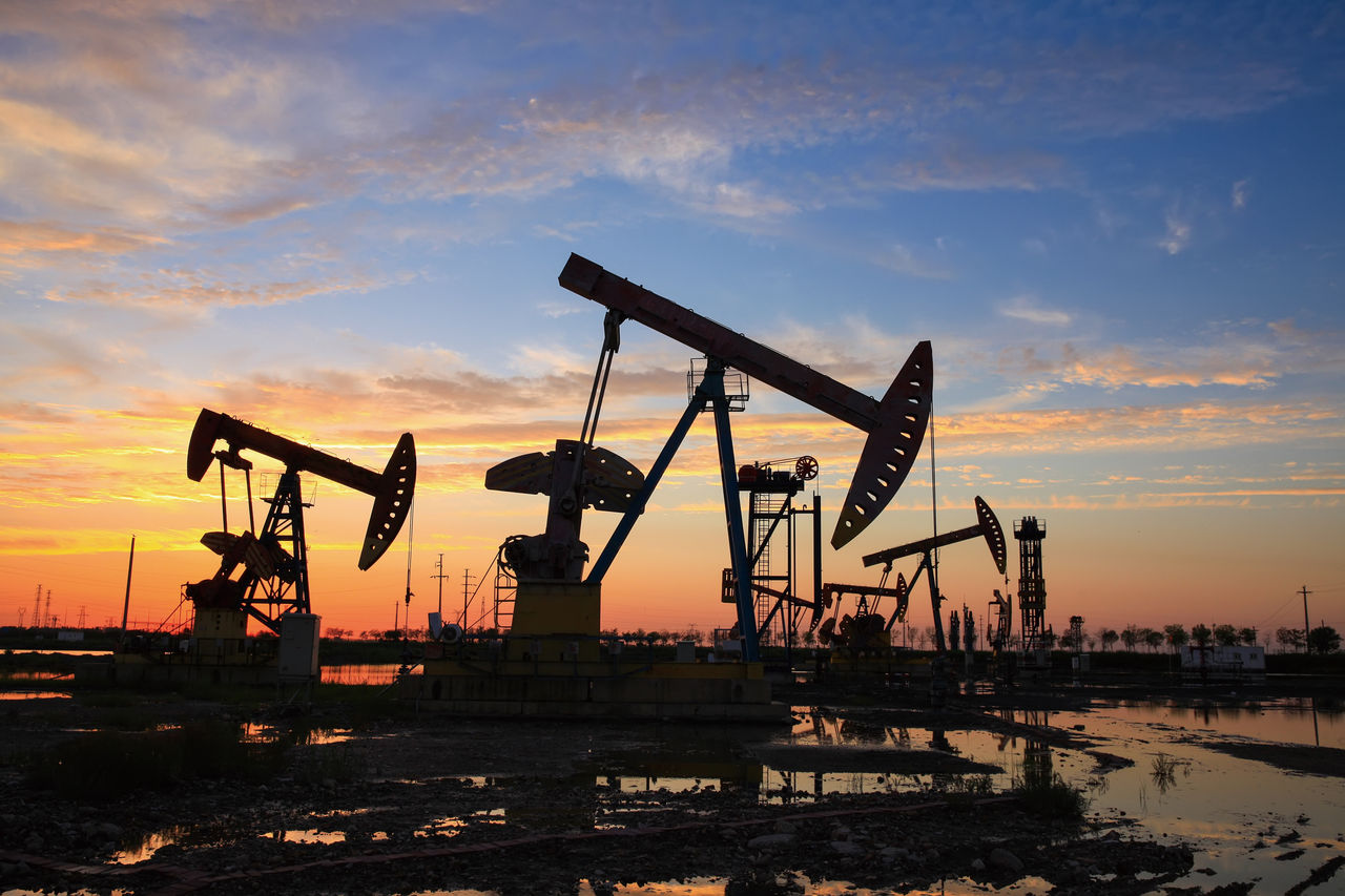 Oil field site, in the evening, oil pumps are running, The oil pump and the beautiful sunset reflected in the water, the silhouette of the beam pumping unit in the evening.