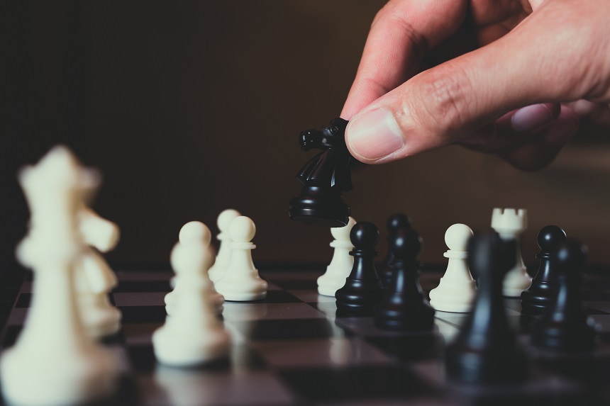 Hand of businessman making move with black knight on chess board, plan and strategy in business concept.