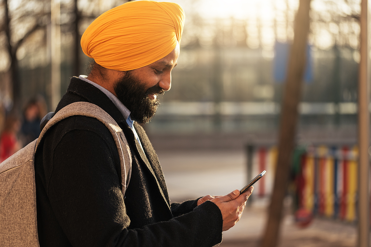 Young handsome Indian Sikh businessman using a cellphone in the street