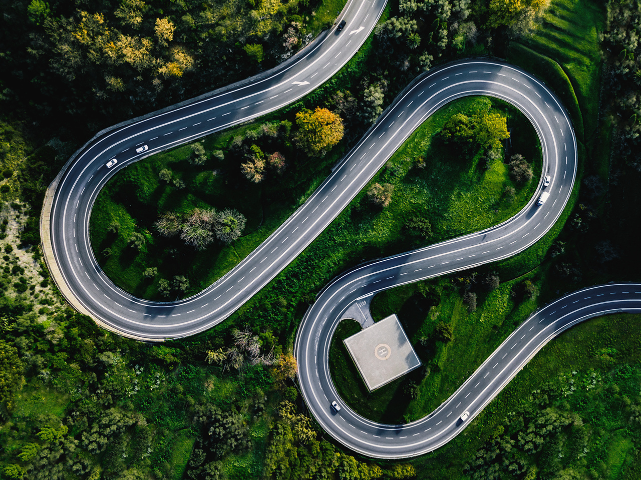Aerial view of winding curved road with helicopter parking in Italy countryside