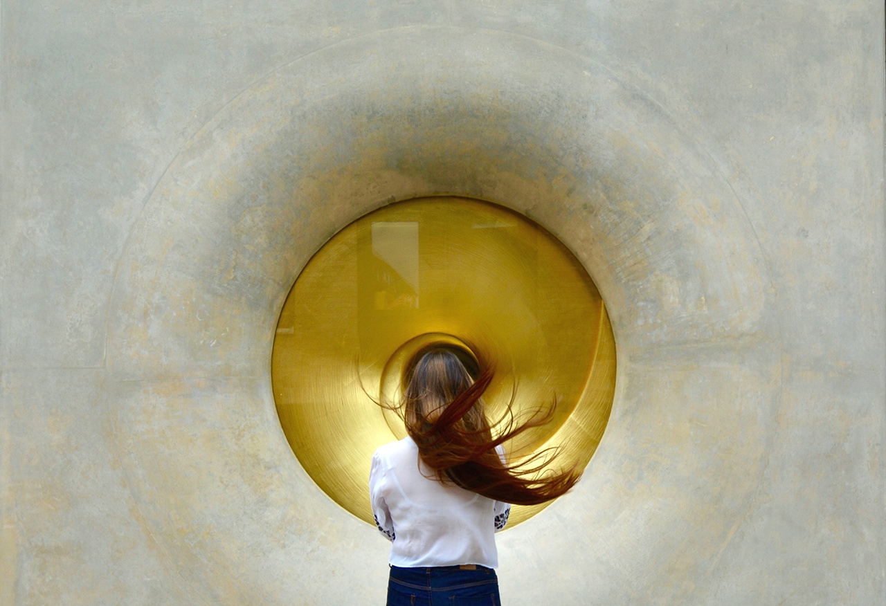 Rear View Of Woman Looking At Gold Circle On Wall