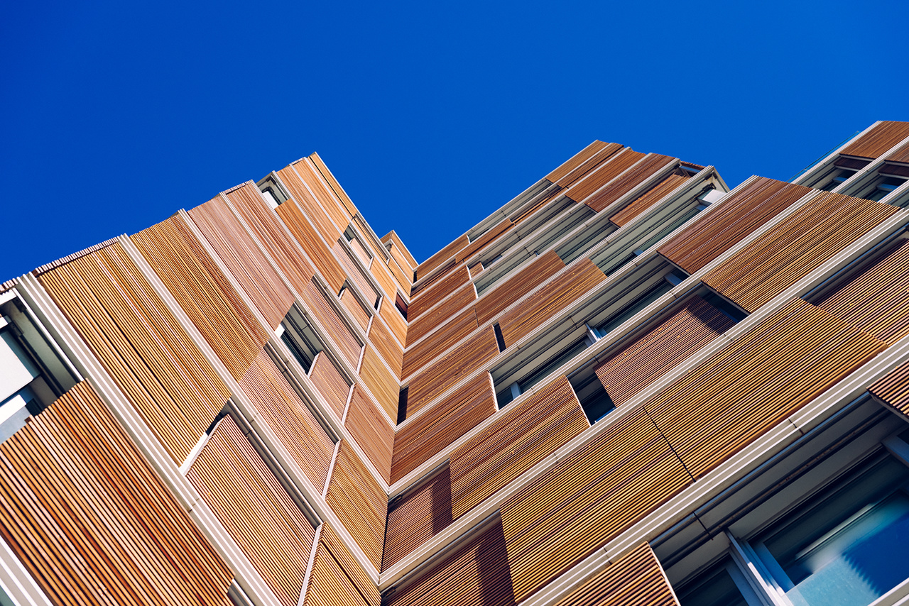 View from the floor of the facade of a modern building clad in ecological wood over clean blue sky, concept of sustainable construction background, copy space.