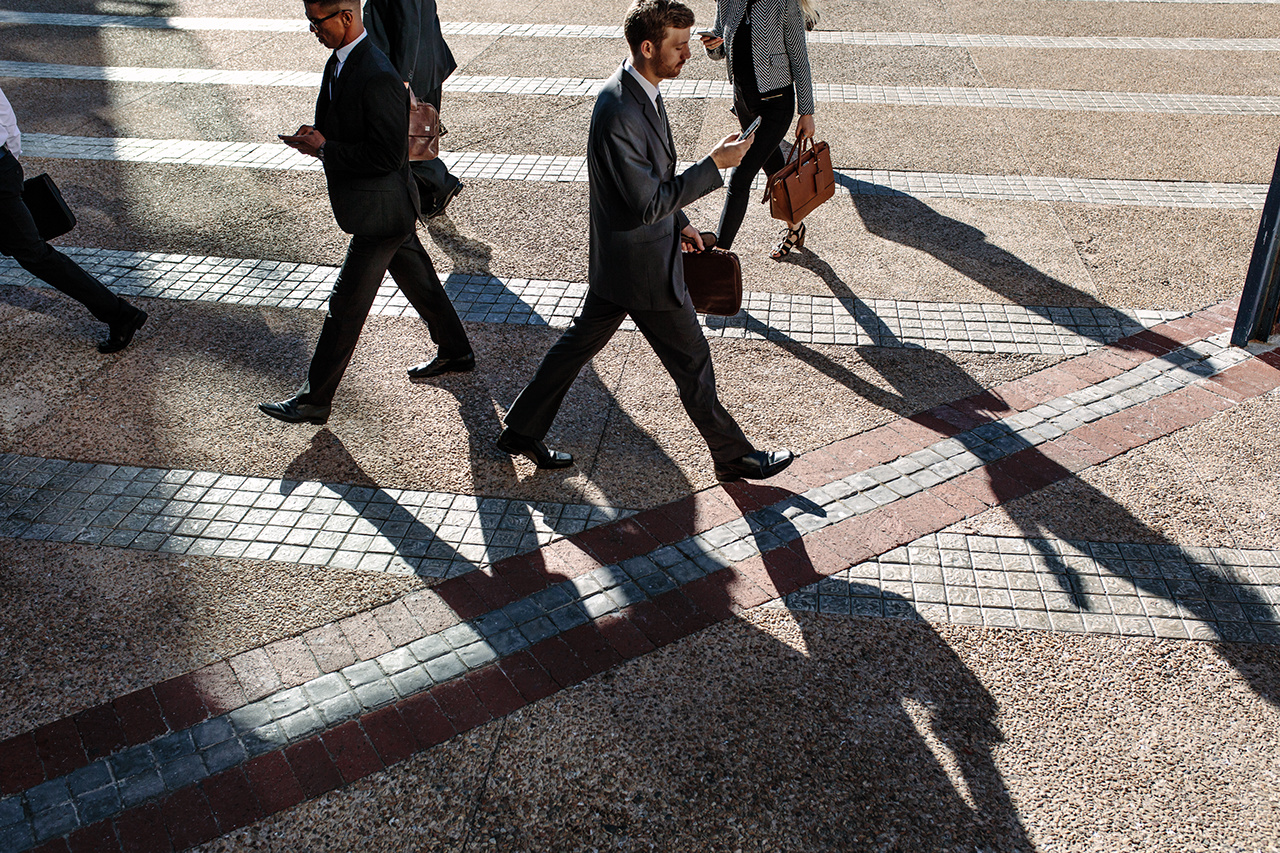 Business people commuting to office in the morning carrying office bags and using mobile phones. Businessmen in a hurry to reach office walking on city street using their mobile phone.