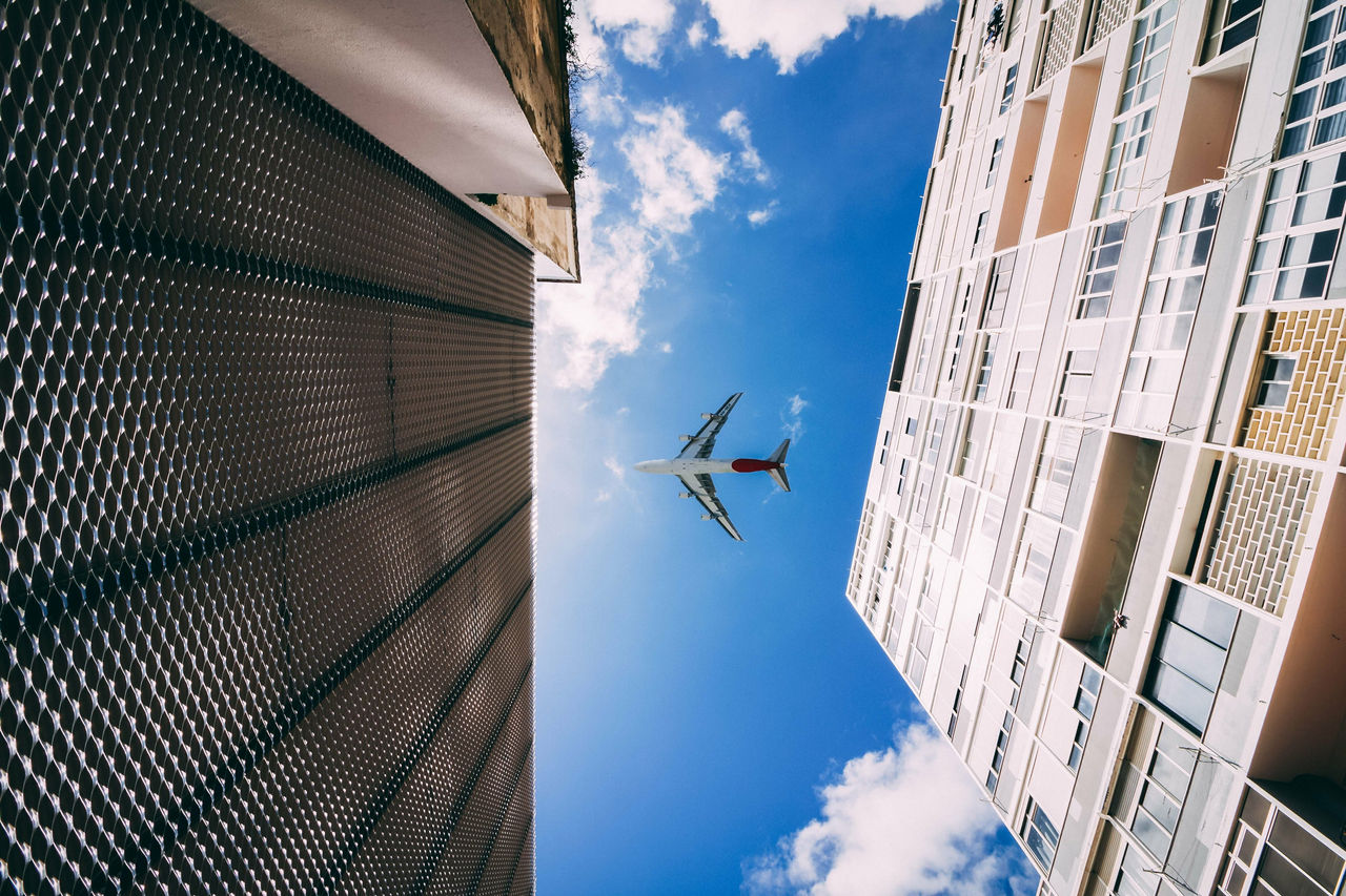 Directly Below Shot Of Buildings And Airplane Flying In Sky
