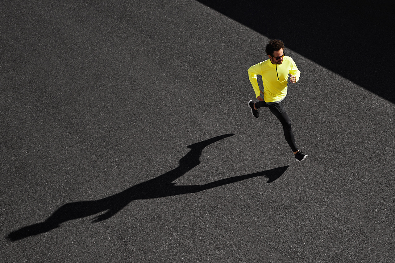 Running man sprinting for success on run. Top view athlete runner training at fast speed at black asphalt. Muscular fit sport model sprinter exercising sprint in yellow sportswear. Caucasian fitness model in his 20s.
