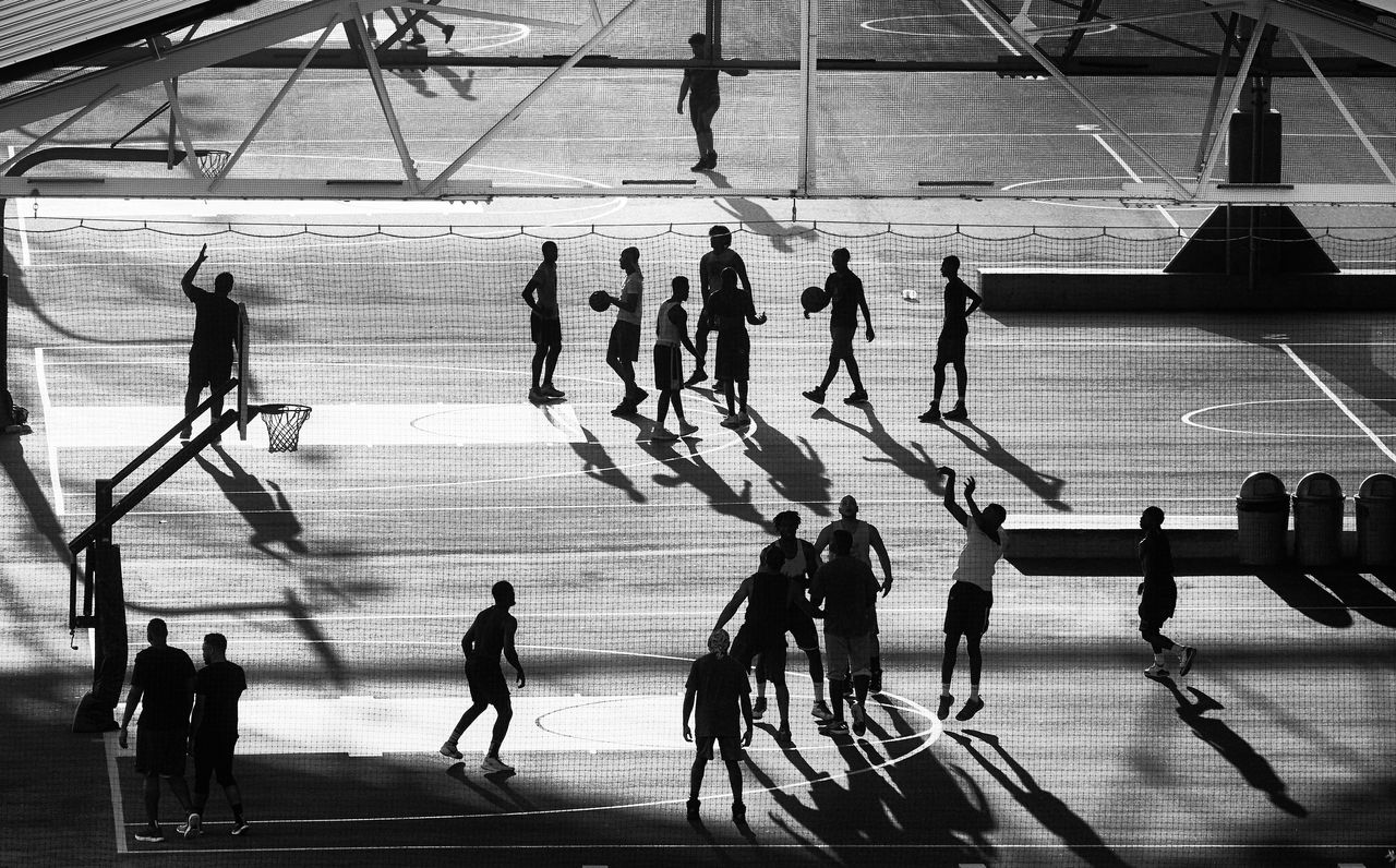 Basketball players silhouettes on Brooklyn pier court at sunset, New York City, USA.