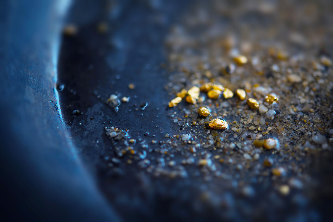 Gold dIscovery. Gold on grungy wash pan with river sand. Gold panning or digging. Very shallow depth of field due to subject size.