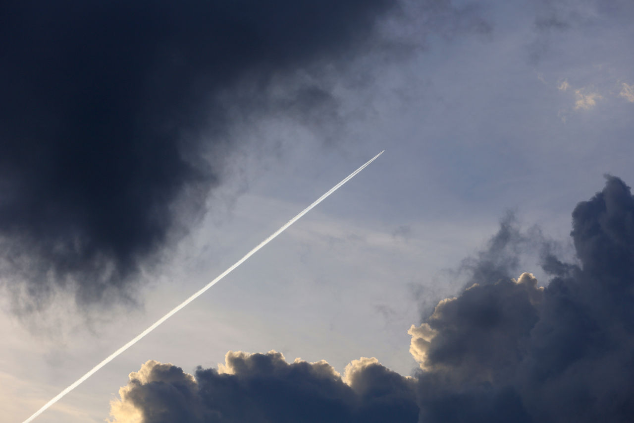 Airplane leaving contrail between dark clouds