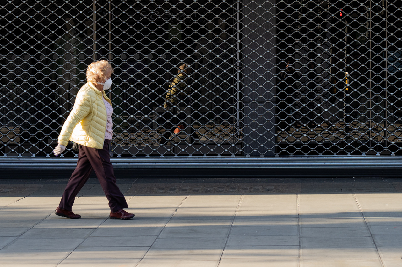 Lady wearing a face mask walking in an empty Oxford Street with closed shutters in the background during coronavirus lockdown