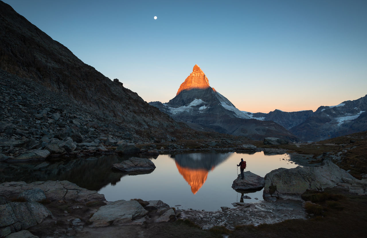 Hiker on a rock in the Riffelsee watching the first sunlight  on the Matterhorn.