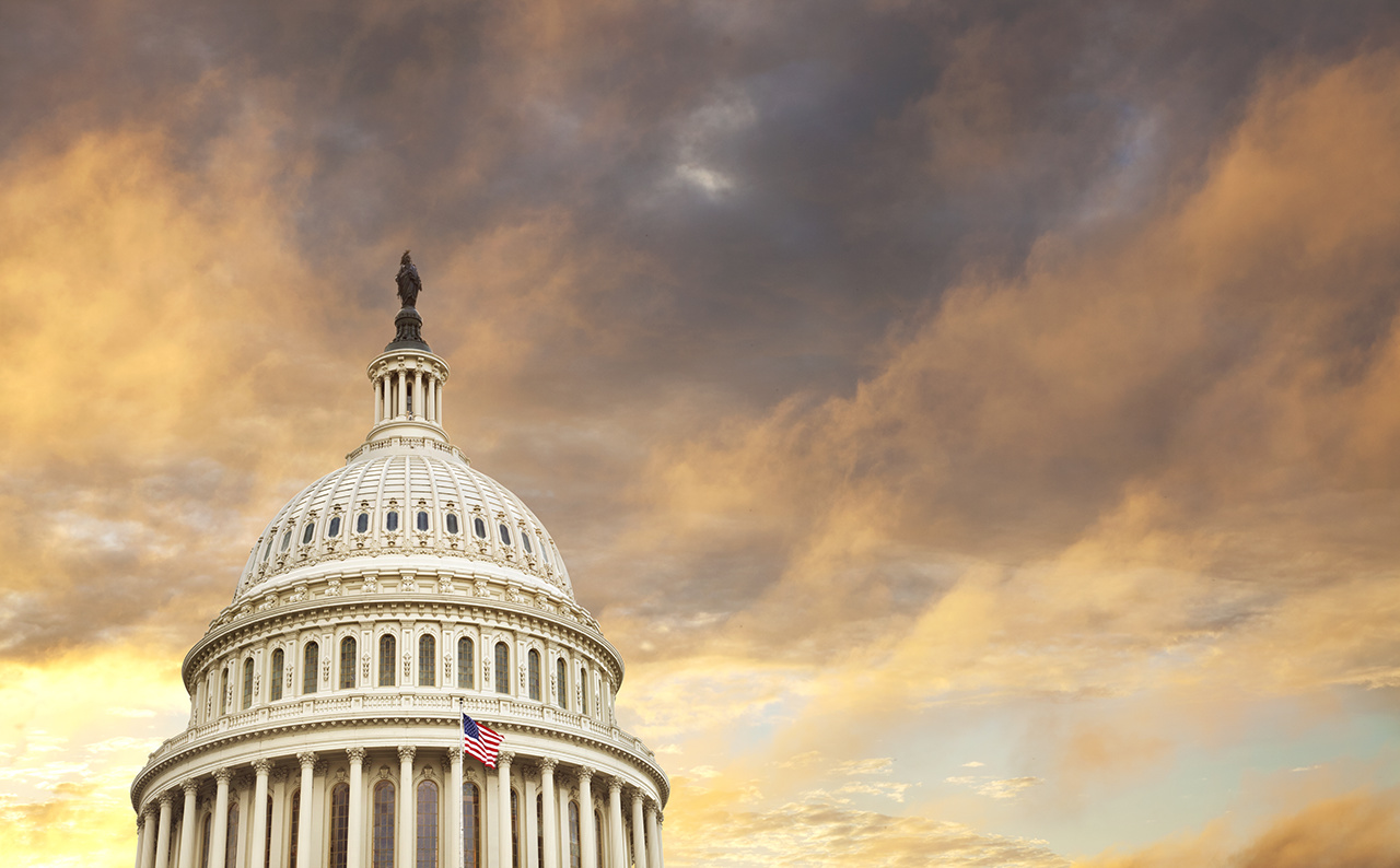 The dome of the United States capitol with an American flag and dramatic clouds behind