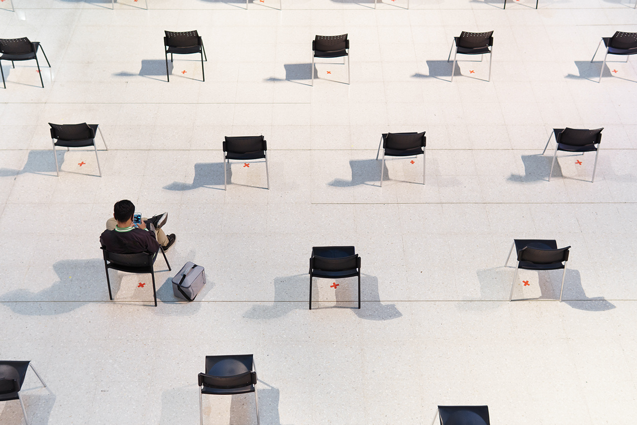 Social distancing, A man sit, chat on smartphone, wait in rows of empty chairs far apart to slow down virus spreading, transmission of disease, reduce contact and infection during pandemic of Covid-19