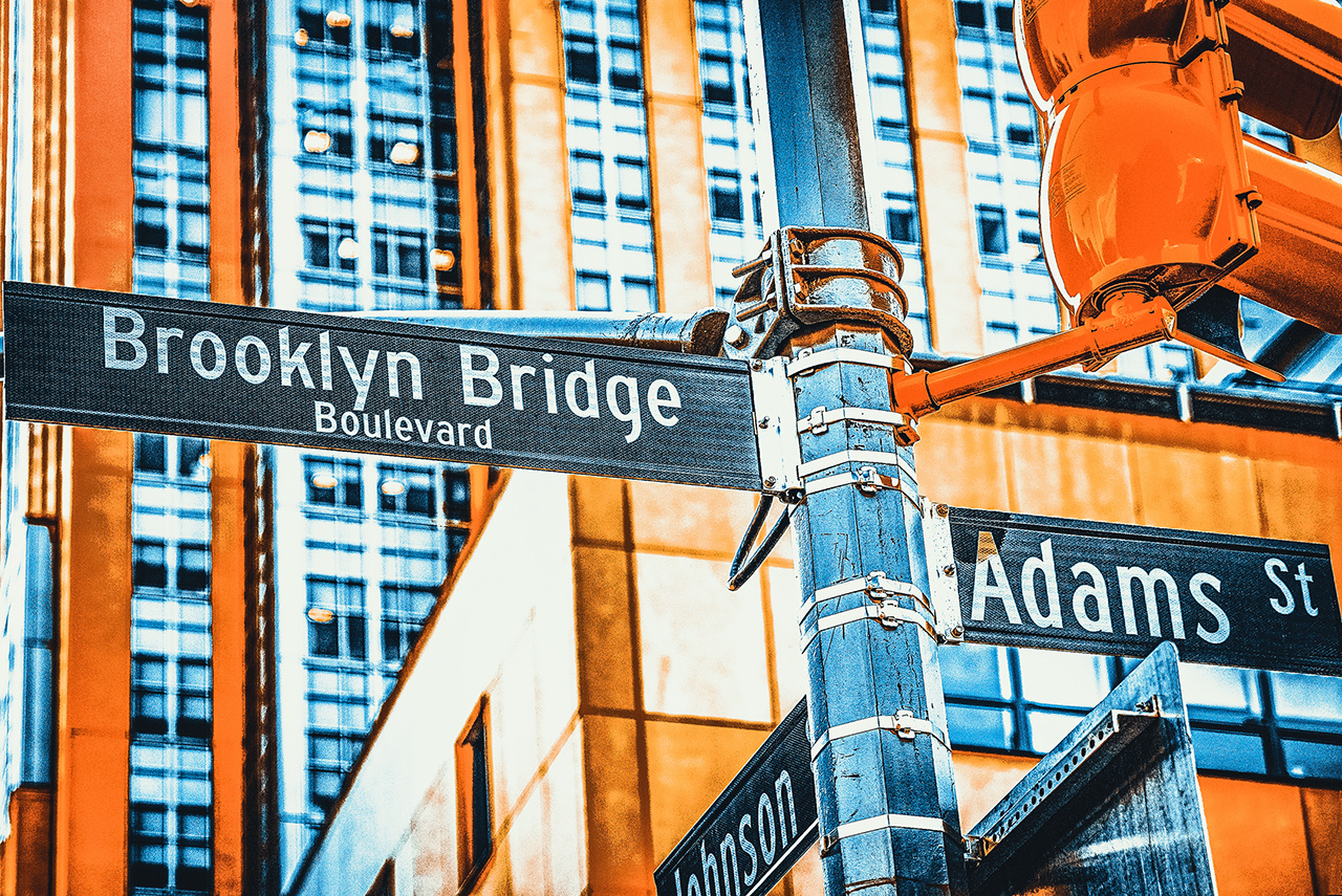 New York, USA- September 08, 2017 : Street sign (nameplate) of Brooklyn Bridge and Adams Street and urban cityscape of New York. Midtown district. 