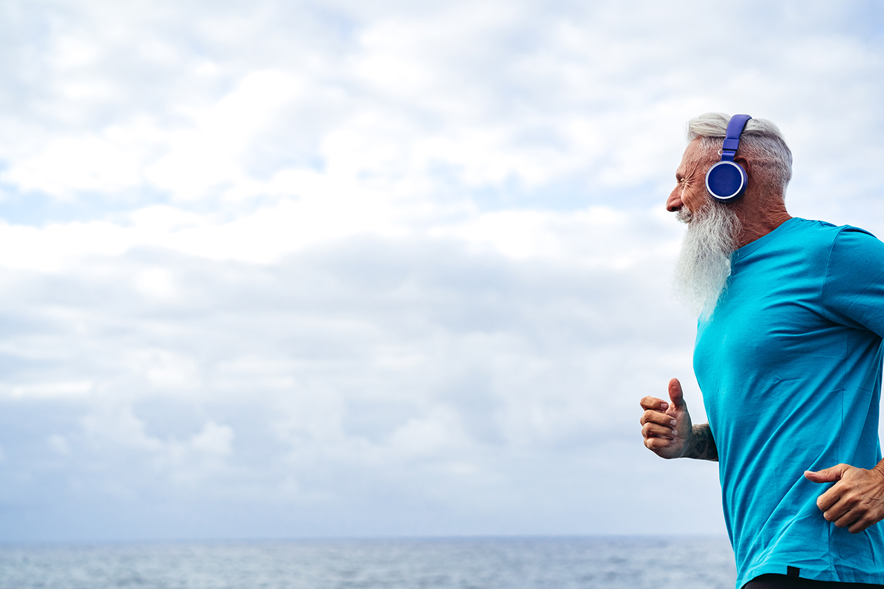 Handsome muscular Caucasian senior man running by the sea with headset on.